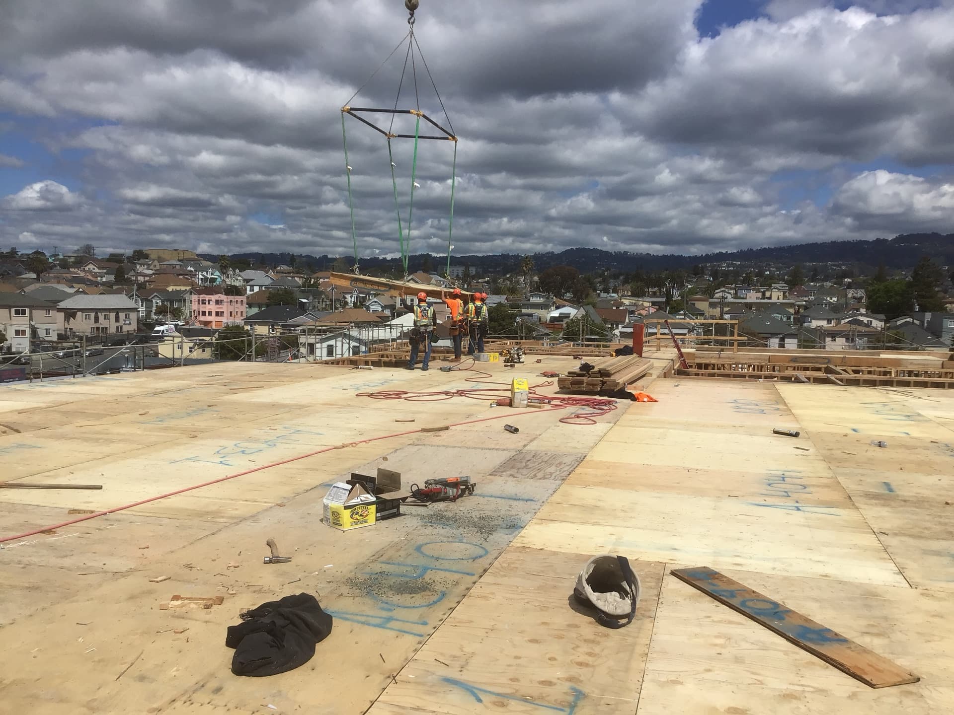 NCC crew on solid sheathed deck receiving crane-lifted panel with dramatic sky and neighborhood view